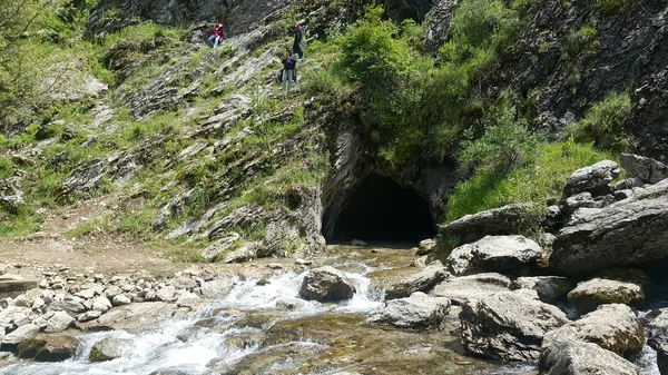 Yeşil bitki örtüsü ve kayalık alanla çevrili Dere ve mağara ağzı görünümü.