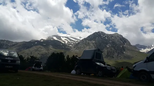 Yemyeşil alanda, karla kaplı zirvelere sahip dağlar ve kamp alanı görünümü.