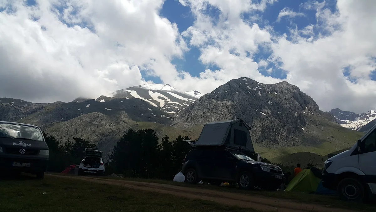 Huzurlu Bir Kamp Deneyimi: Dedegöl Dağı'nın Karla Kaplı Zirveleri Yemyeşil alanda, karla kaplı zirvelere sahip dağlar ve kamp alanı görünümü.