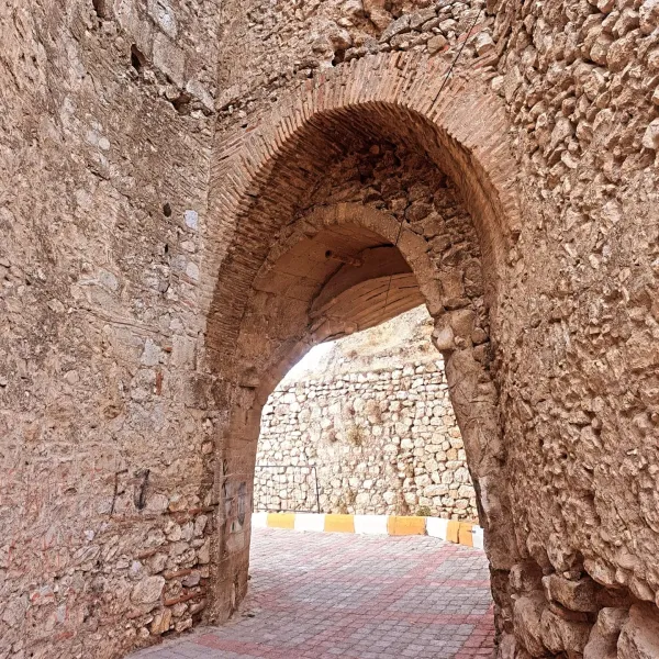 Büyük kemerli kapı ile çevrili taş duvarlar ve doğal alan.