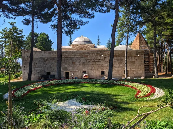 Yeşil alanda yer alan taş duvarlı tarihi Ertokuş Medresesi, çiçek tarhı ve ağaçlarla çevrili.