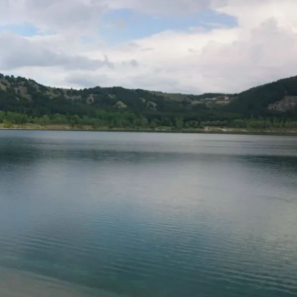 Sakin bir gölde hafif dalgalar, yemyeşil dağlar ve bulutlu gökyüzü