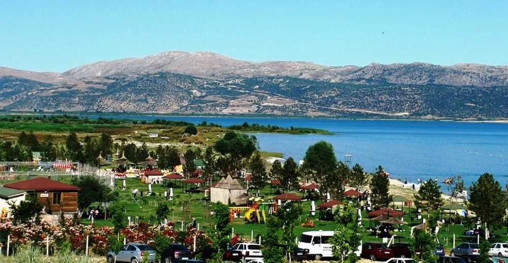 Yalvaç Taşevi Plajı'nda göl manzarası, yeşil alanlar ve piknik alanları görülüyor.