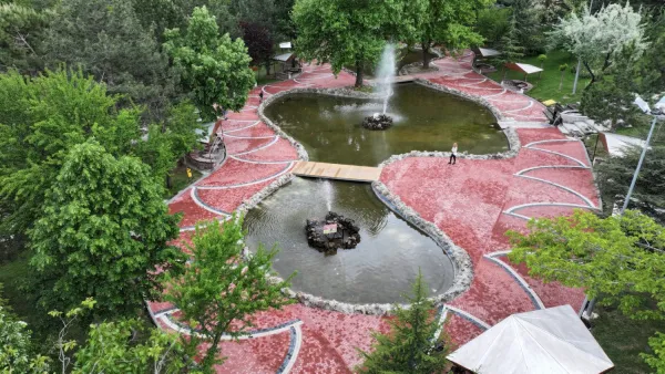 Yeşil ağaçlarla çevrili parkta gölet ve yürüyüş yolları görünmekte.