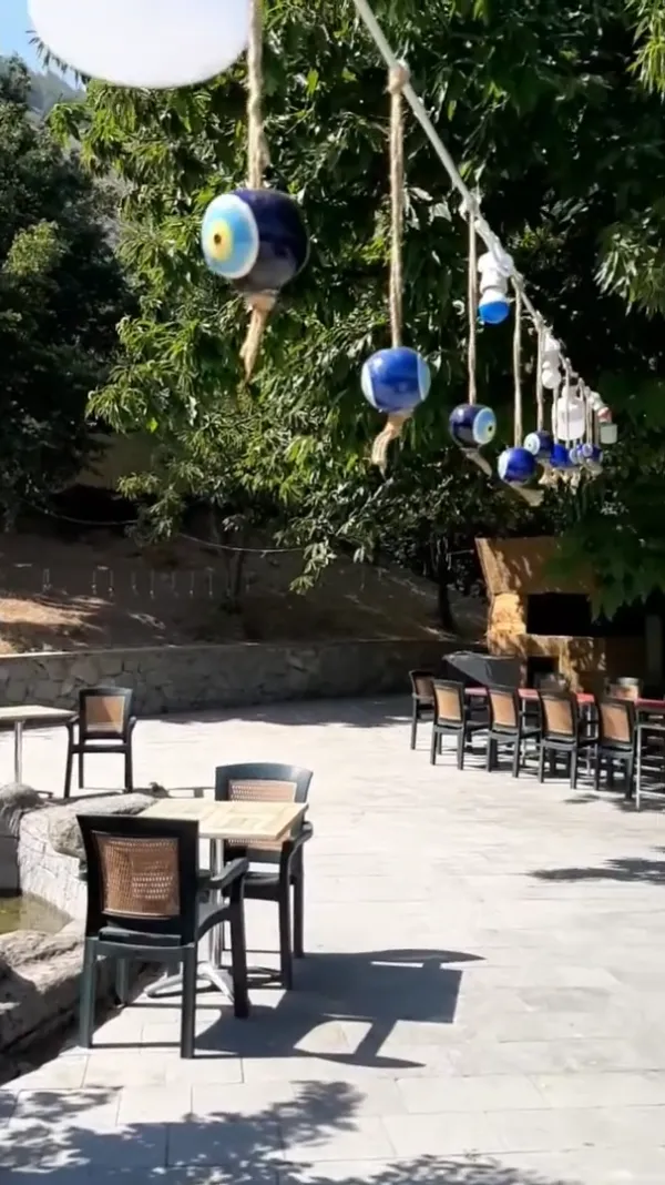 Yeşil ağaçlarla çevrili, şans gözleriyle süslenmiş sakin bir restoran alanı.