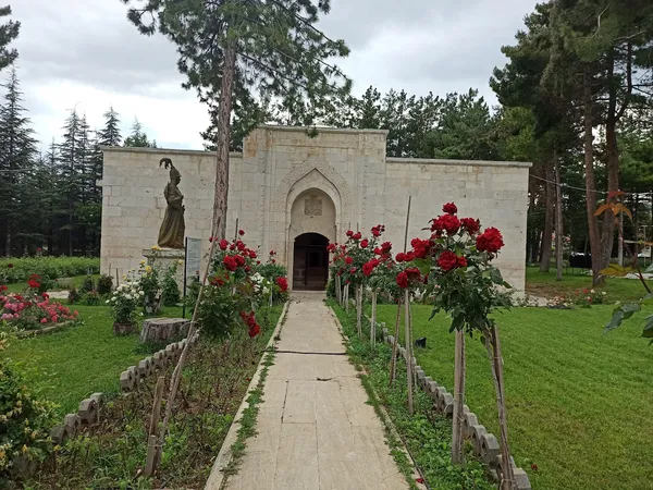 Yeşil bahçede taş yapı, açık kapı, renkli güller ve genç bitkiler.