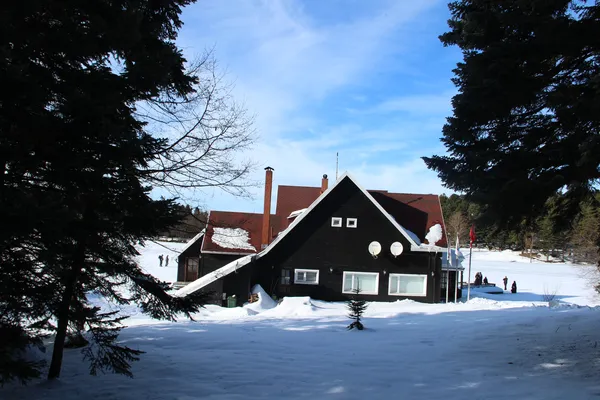 Karla kaplı alanda küçük bir yapı ve yürüyen insanlar, mavi gökyüzü.