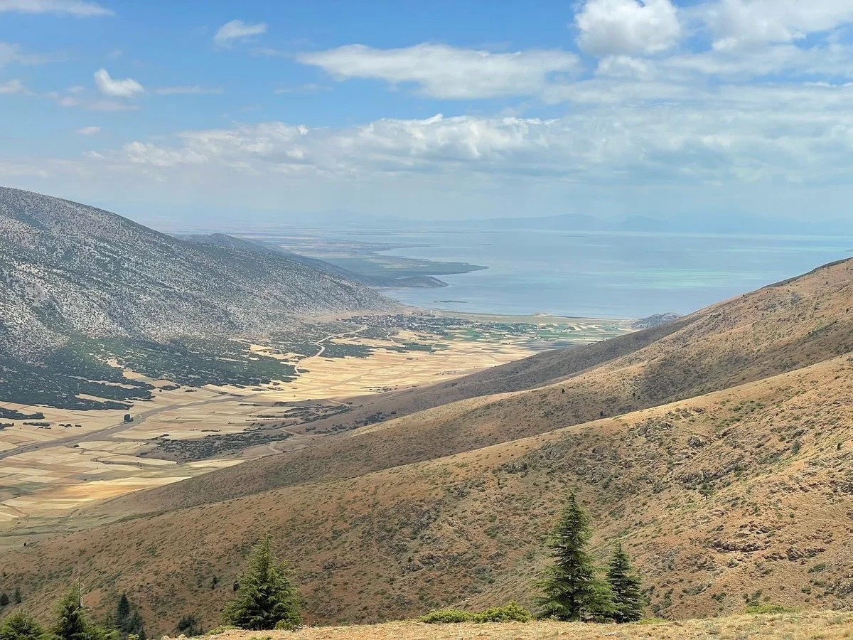 Dağlık alanda sarımsı tahıllı araziler ve yeşil alanlarla birleşen deniz manzarası.