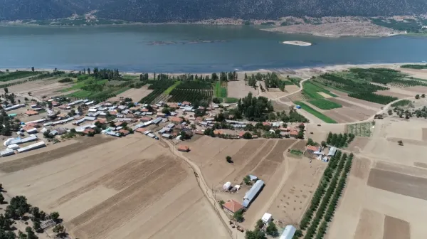 Köy, göl kenarında ve dağların eteklerinde yer alıyor; yeşil tarım alanları ve toprak yollarla çevrili.