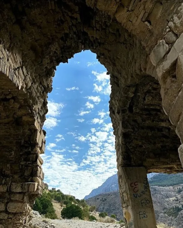 Kemerli geçit, mavi gökyüzü ve yeşil dağlarla çevrili tarihi taş yapılar