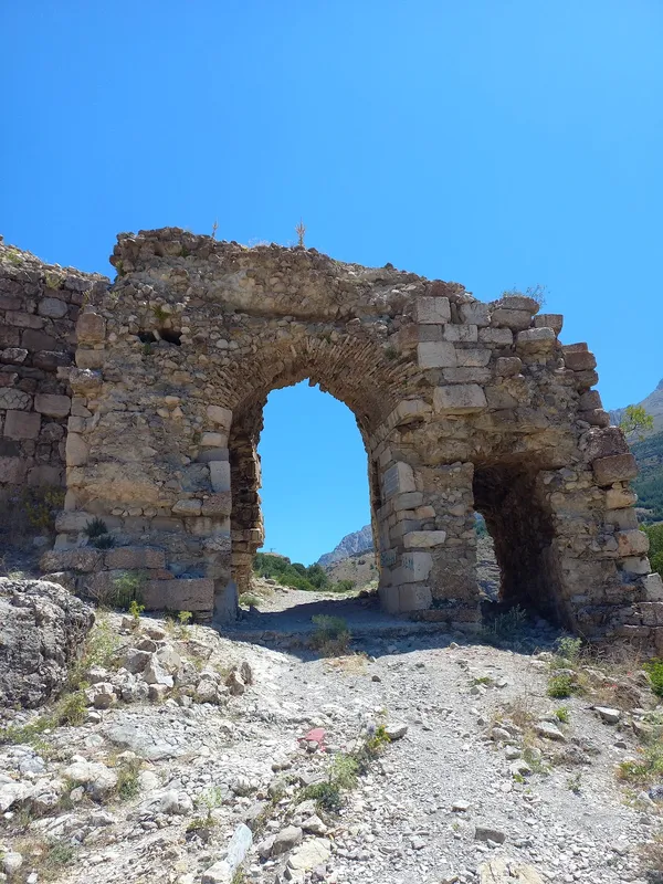Büyük taş kemer, eski kalıntılar ve etrafındaki doğal peyzaj.