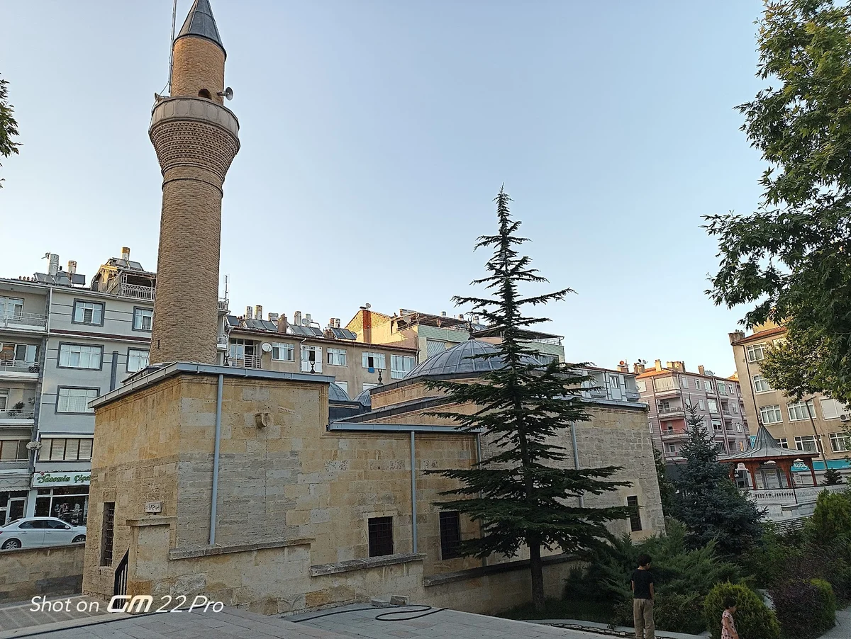 Doğanın Kucağında Tarih - Taş ve Ağaçlarla Yunus Emre Türbesi Yunus Emre Türbesi'nin taş cephe detayları ve yüksek minaresi, yeşil ağaçlarla çevrili bir ortamda.