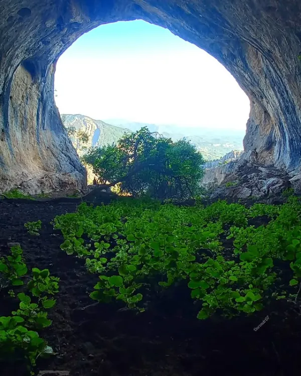Geniş doğal mağara açıklığından mavi gökyüzü ve dağ silueti görünümü