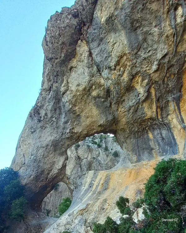 Büyük doğal taş kemer, sarımsı ve açık gri tonlarında, arka planda dağ silueti ile yeşil bitki örtüsü