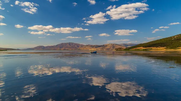 Sakin göl, açık mavi gökyüzü ve dağ manzarasıyla huzur veriyor.