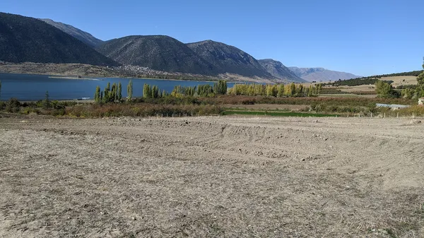 Etrafı dağlarla çevrili, sarı yapraklı ağaçlarla dolu göl manzarası.
