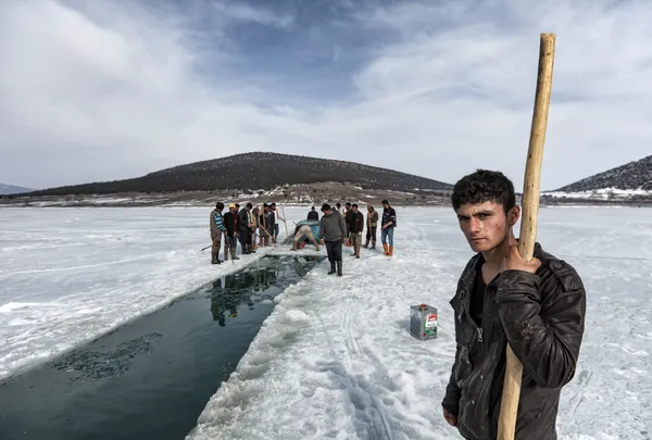 Kış mevsiminde donmuş gölet üzerinde balık tutmaya çalışan insanlar ve dağ manzarası.