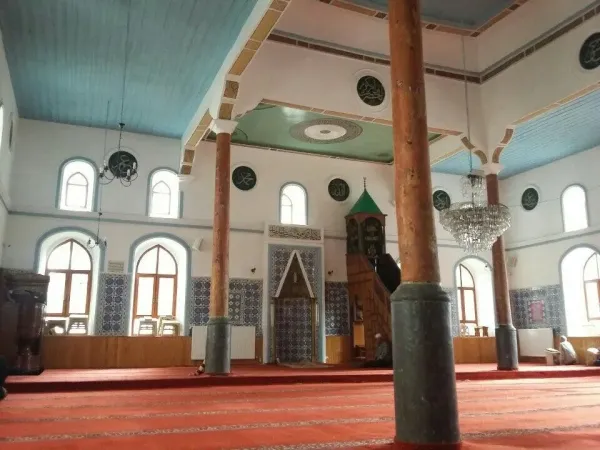 Açık mavi tavan, büyük avize ve çini desenleriyle süslenmiş cami iç mekanı.