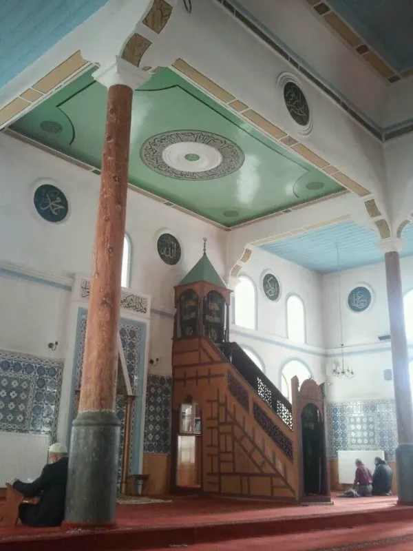 Açık mavi ve yeşil süslemeli tavan, ahşap minber ve dua eden insanlar