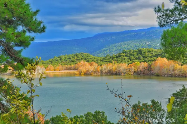 Sakin bir göl, çevresindeki sonbahar renkleriyle bezenmiş ağaçlar ve mavi dağlar.