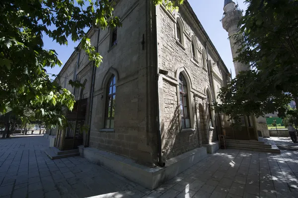 Tarihi taş cami ve yüksek minaresi, çevresindeki yeşil ağaçlarla aydınlık bir günde görünmekte.