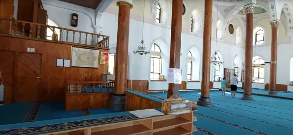 Geniş cami iç mekanında mavi halı, yüksek tavan ve sütunlar görünmekte.