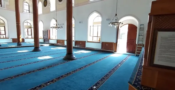 Aydınlık cami iç mekanında mavi halılar ve ahşap sütunlar görünmekte.