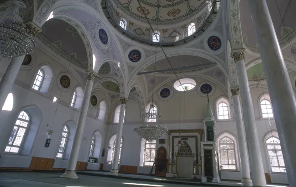 Yüksek tavanlı cami iç mekanında renkli kubbe ve Arapça yazılar