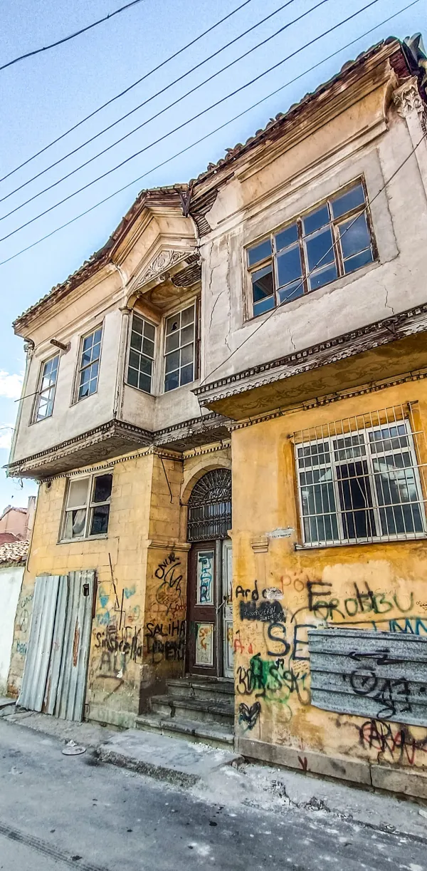 İki katlı sarı dış cepheli tarihi bina, çoklu panjurlu pencereler ve süslü kemerli girişle dikkat çekiyor.