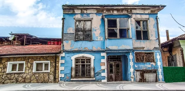 Mavi dış cepheli tarihi bina, büyük kapı ve geniş pencerelerle ön planda.