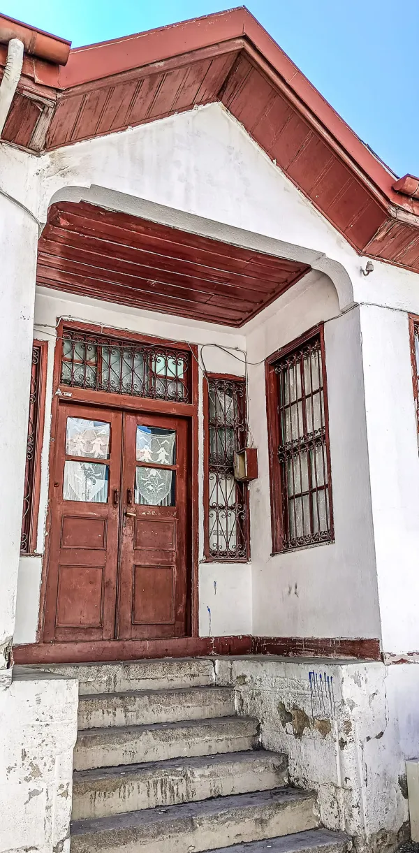 Beyaz duvarlı tarihi bir evin kırmızı çatılı girişi ve ahşap kapısı