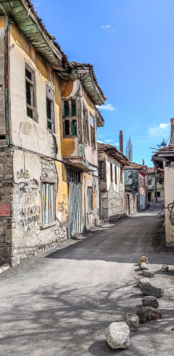 Eski sokakta, yarı yıkılmış tarihi Isparta evleri ve grafitilerle dolu duvarlar görünmekte.