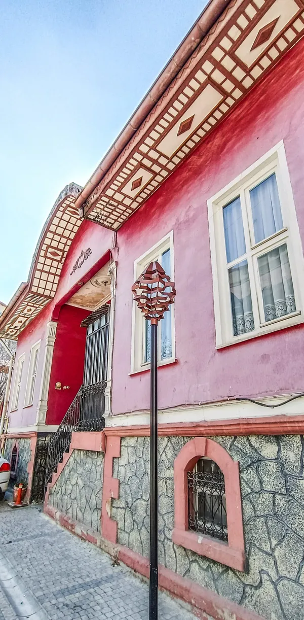 Pembe dış cepheye sahip tarihi bir Isparta evi, detaylı çatı ve balkon ile öne çıkıyor.
