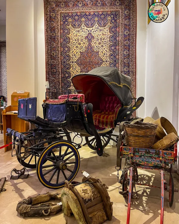 Geleneksel atlı araba, kadife kaplama oturak, halı ve nostaljik eşyalarla dolu bir müze ortamı.