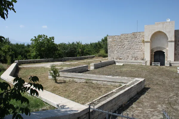 Ertokuş Hanı'nın taş duvarları, yeşil ağaçlar ve düzenlenmiş boş alanlar.