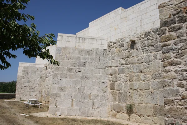 Eski taş yapının önünde ahşap masa ve sandalyeler, arka planda modern bir bölüm.