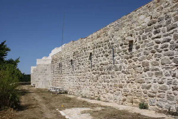 Antik taş duvar, açık mavi gökyüzü ve yeşil alanla çevrili.