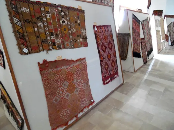 Sergi alanında asılı geleneksel kumaşlar ve halılar, renkli ve desenli dokuma eserler.