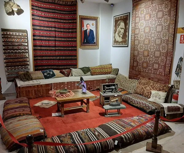 Geleneksel oturma alanında renkli halılar, masa ve sanat eserleri yer alıyor.