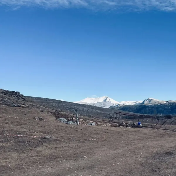 Geniş açık arazide uzaktaki dağ silüeti, toprak zemin ve çalılıklar görünmekte.