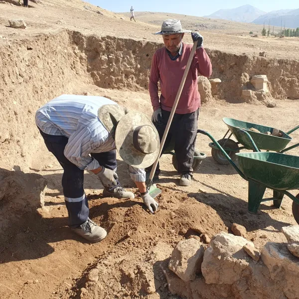 Arkeolojik alanda çalışan iki kişi, toprak kazıyor ve etraflarında taşlar var.