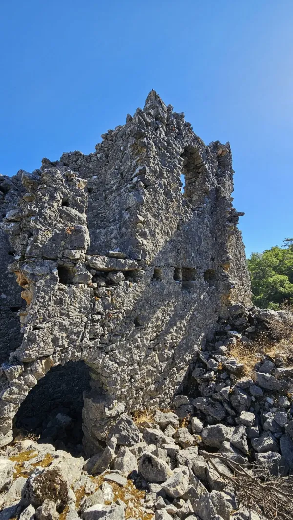 Yarı harabe taş yapı, çökmüş duvarlar ve açık mavi gökyüzü.