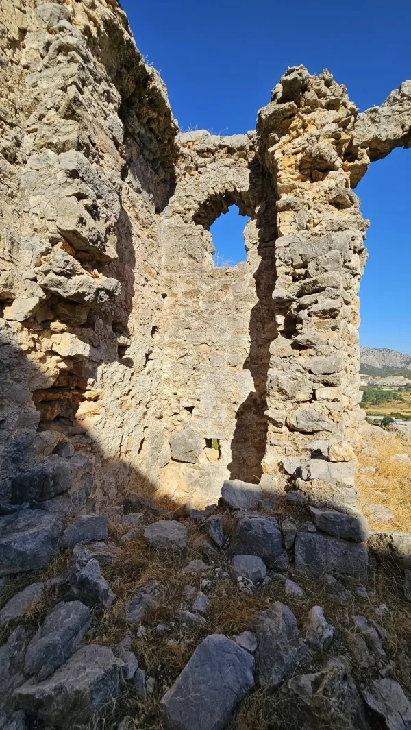 Eski taş kalıntıları, erimiş duvarlar ve sararmış çimenler ile tarihî manzara.