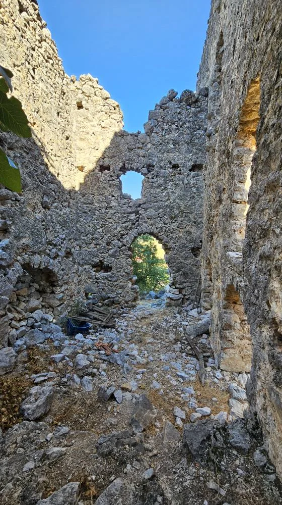 Eski taş kalıntıları, yüksek duvarlar ve yeşil bitkilerle çevrili doğal bir ortam.