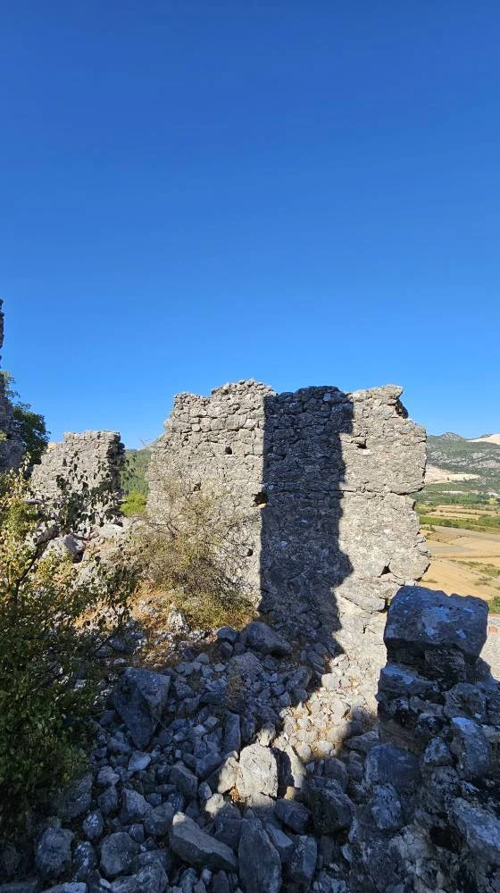 Taş yapılar ve harabe kalıntıları ile çevrili yeşil dağlar ve mavi gökyüzü