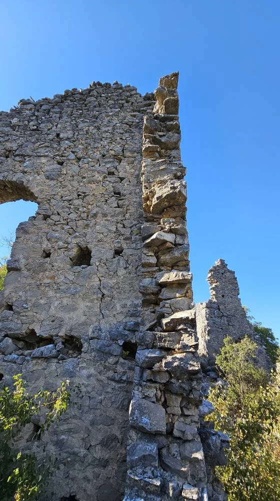 Eski taş kalıntıları, çatlaklarla dolu yüksek duvar ve yeşilliklerin arasında kalmış yapılar.