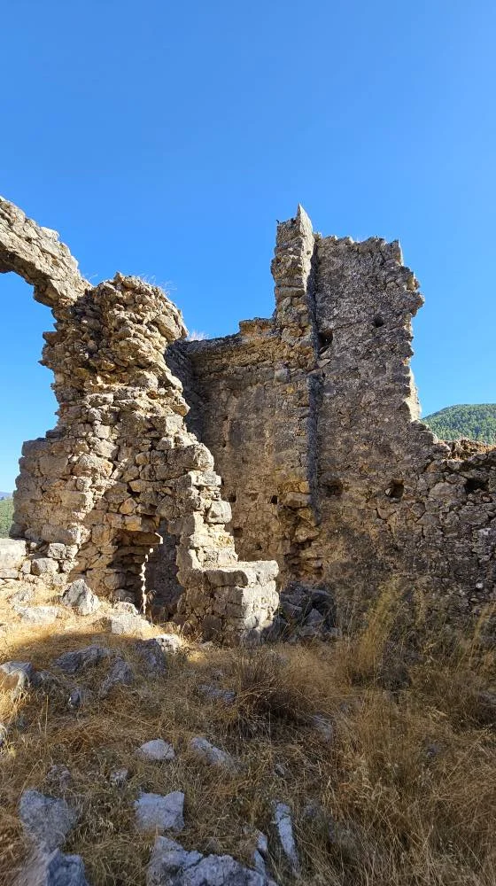 Taşlarla inşa edilmiş tarihi kalıntılar, mavi gökyüzü ve sarı otlarla çevrili.