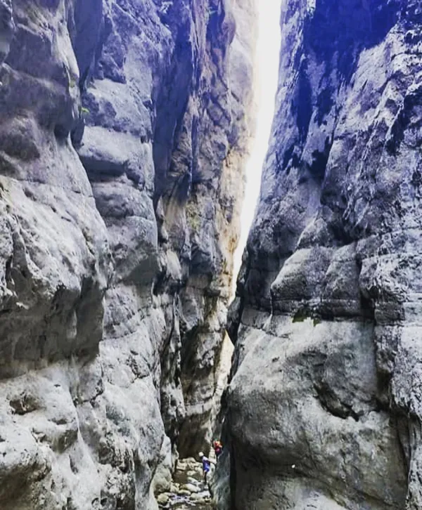 İki kayalık arasında dar bir kanyon, yürüyüş yapan iki kişi ve ışık huzmeleri.