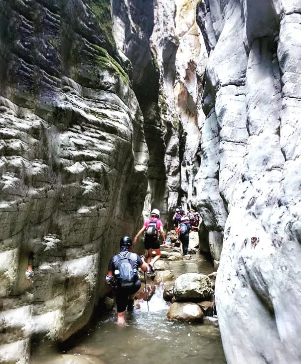 Dar kayalık kanyon içinde gruplar halinde yürüyen insanlar, sırt çantaları ve kasklarıyla doğa yürüyüşü yapıyo