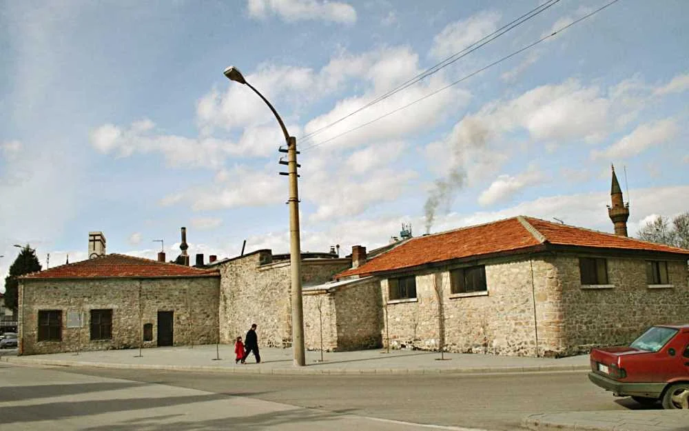 Dalboyunoğlu Hamamı'nın Tarihi İzleri - Eski Taş Yapılar ve Minare! Eski taş yapılar, cami minaresi ve yürüyen insanlar ile tarihi bir yerleşim alanı.
